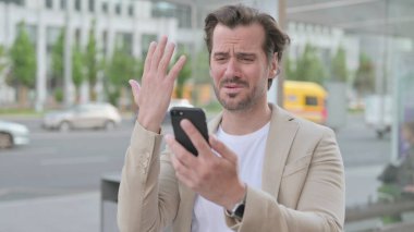 Man Reacting to Loss on Smartphone Outdoor