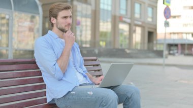 Orta yaşlı bir adamın Bench 'te otururken dizüstü bilgisayar kullandığını düşünüyorum.