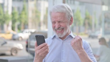 Senior Old Man Celebrating Online Success on Smartphone Outdoor