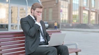 Coughing Middle Aged Businessman Using Laptop while Sitting Outdoor on Bench