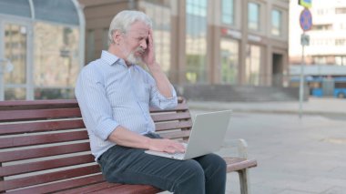Senior Old Man with Headache Using Laptop while Sitting Outdoor on Bench