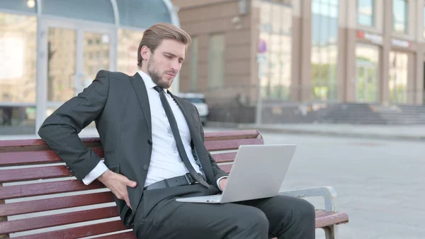 Middle Aged Businessman with Back Pain Using Laptop while Sitting Outdoor on Bench