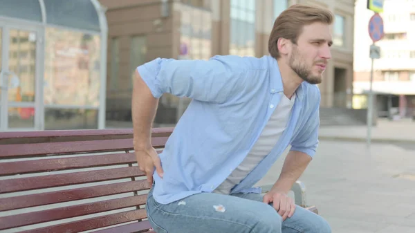 Middle Aged Man having Back Pain while Sitting on Bench Outdoor