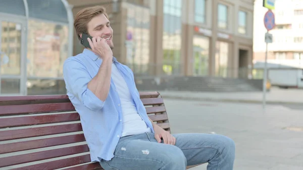 Middle Aged Man Talking on Phone while Sitting Outdoor on Bench