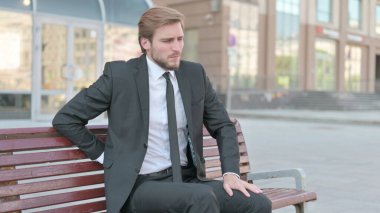 Middle Aged Businessman having Back Pain while Sitting on Bench Outdoor