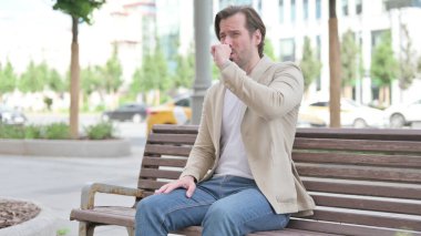 Man Coughing while Sitting on Bench