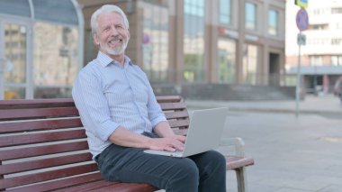 Senior Old Man Pointing at the Camera while Sitting on Bench Outdoor