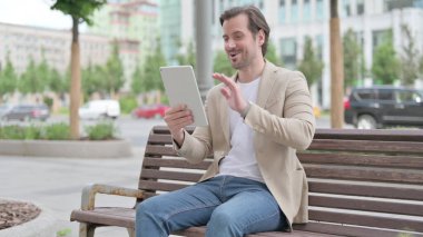 Online Video Chat on Tablet by Man Sitting on Bench