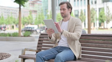 Man using Tablet while Sitting on Bench