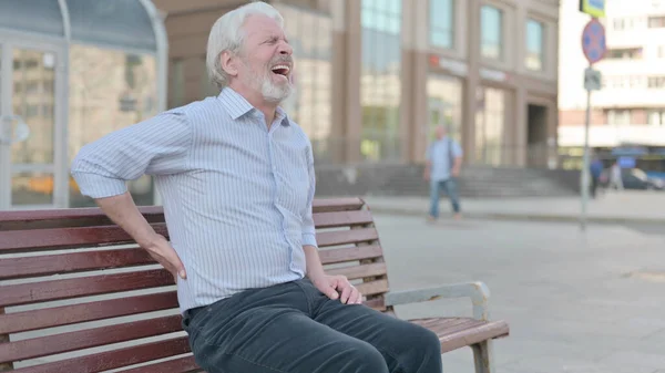 Senior Old Man having Back Pain while Sitting on Bench Outdoor