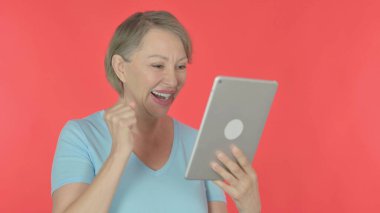 Senior Old Woman Celebrating Success on Tablet on Red Background