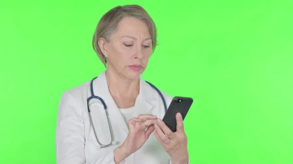 Senior Female Doctor Browsing Smartphone Green Background — Zdjęcie stockowe
