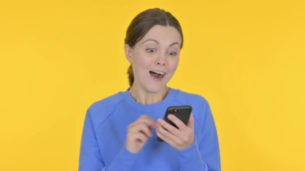 在黄色背景下 在智能手机上欢庆的女性 — 图库视频影像