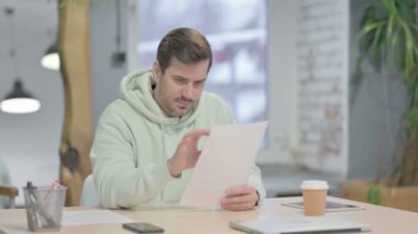 Young Adult Man Celebrating Success while Reading Documents in Office