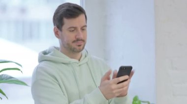 Young Adult Man Using Smartphone while Standing Near Window