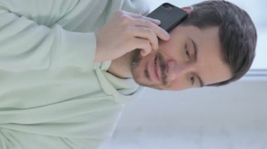 Vertical Video of Young Adult Man Talking on Phone while Standing Near Window