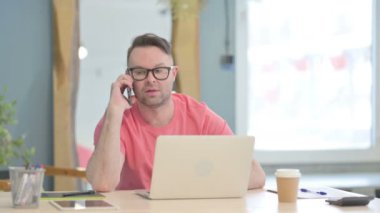 Displeased Young Adult Man Talking Angrily on Smartphone at Work