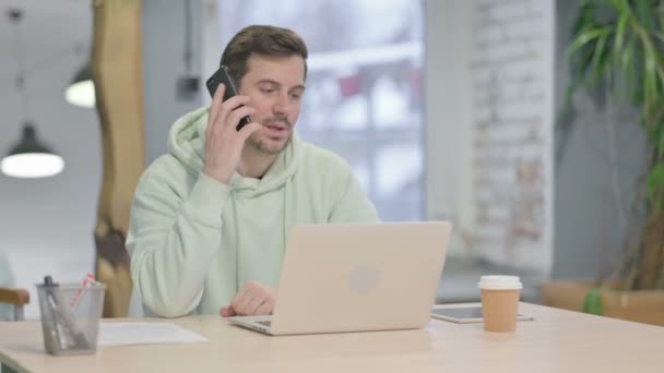 Hombre Adulto Joven Hablando Por Teléfono Mientras Usa Ordenador Portátil — Vídeos de Stock