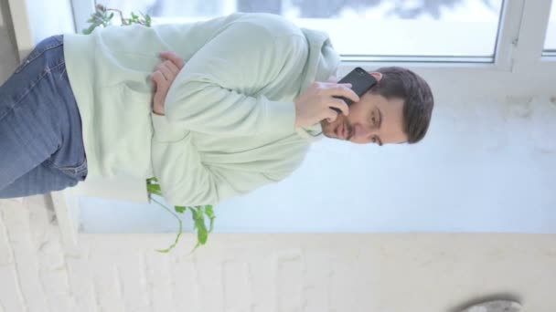Vertical Video Young Adult Man Talking Phone While Standing Window — Stockvideo