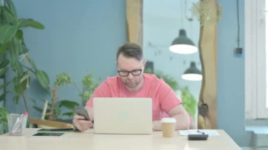Creative Senior Old Man using Phone while Working on Laptop