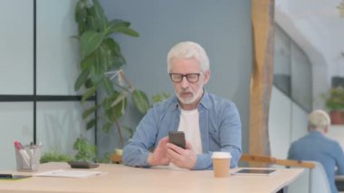 Senior Old Man Browsing Internet on Smartphone at Work