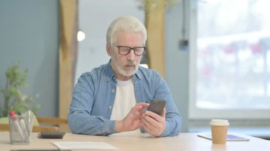 Kıdemli ihtiyar ofiste akıllı telefon kullanıyor.