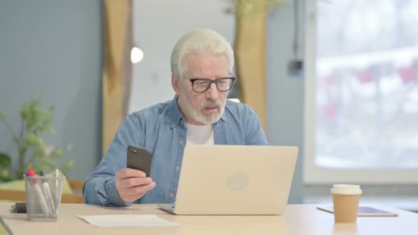 Vanhempi Mies Joka Käyttää Puhelinta Kannettavaa Tietokonetta Työhön — kuvapankkivideo