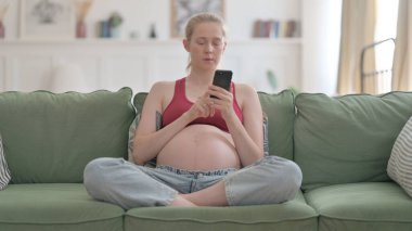 Pregnant Woman Browsing Internet on Smartphone at Home