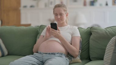 Pregnant Woman Browsing Smartphone while Sitting on Sofa