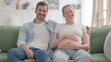 Pregnant Woman with Husband Smiling while Holding Her Tummy