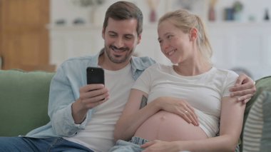 Pregnant Couple Using Smartphone while Sitting on Sofa