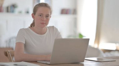 Ofiste dizüstü bilgisayar kullanırken Genç Kadın Kameraya Bakıyor