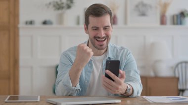 Successful Casual Man Celebrating on Smartphone in Office
