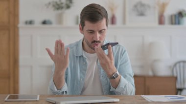 Upset Casual Man Talking Angrily on Smartphone in Office