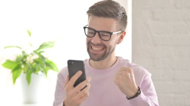 Genç Yetişkin Adam Akıllı Telefon 'da Başarı Kutlaması
