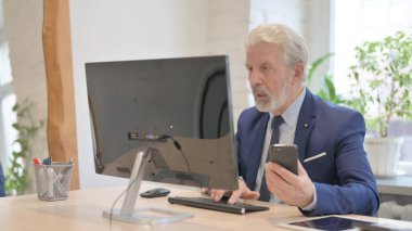 The Old Businessman Working on Smartphone and Computer