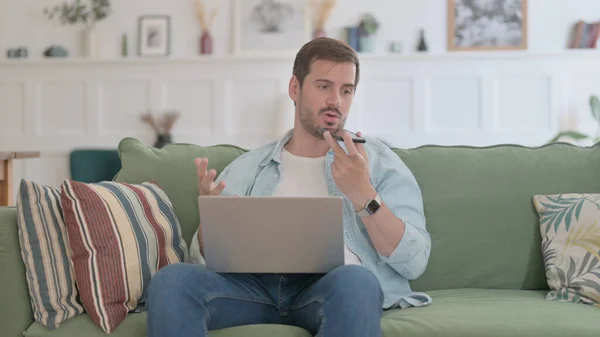 Angry Casual Man with Laptop Talking on Phone on Sofa