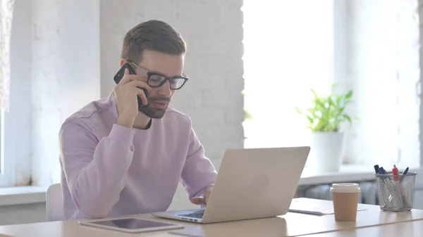 Jonge Volwassen Man Praten Telefoon Tijdens Het Gebruik Van Laptop — Stockfoto