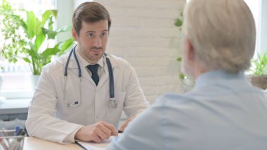 The Young Doctor Talking with Old Patient in Clinic