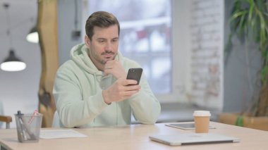 Young Adult Man Browsing Internet on Smartphone in Office