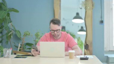 Creative Adult Man using Smartphone while using Laptop