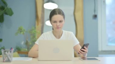 Young Woman using Phone and Laptop for Work