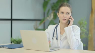 Laptop kullanırken telefonda konuşan genç bayan doktor.