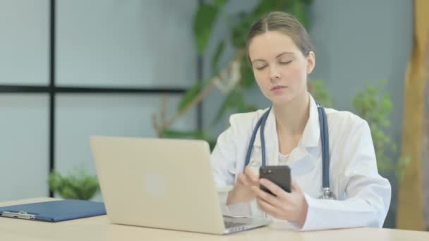 年轻女医生在使用笔记本电脑时使用智能手机 — 图库视频影像