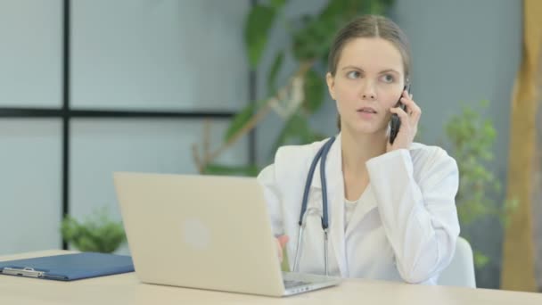 年轻的女医生一边打电话一边用笔记本电脑 — 图库视频影像