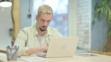 Dizüstü bilgisayarda, boyun ağrısında çalışan yorgun genç adam.