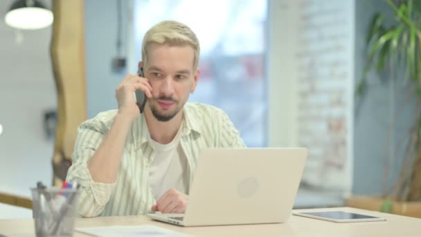 Unge Man Pratar Telefon Och Använder Laptop — Stockvideo