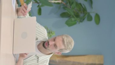 Akıllı telefon ve dizüstü bilgisayarda çalışan genç adamın dikey videosu