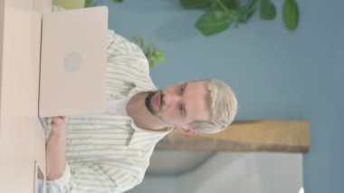 Dizüstü bilgisayar kullanırken Ciddi Genç Adam 'ın Kameraya Bakışının Dikey Videosu