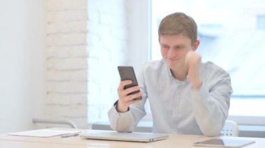 Young Businessman Celebrating Win on Smartphone